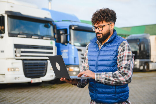 Man using laptop checking logistics data near trucks