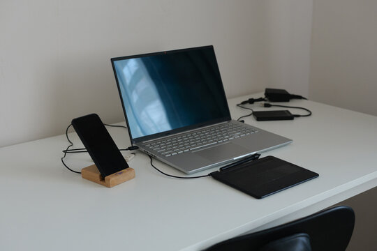 A sleek, modern workspace showcases a laptop and smartphone on a wooden stand. A tablet lies near the laptop, with a few visible cables, creating a tidy setup - Powered by Adobe
