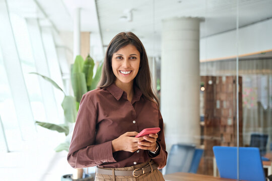 Portrait latin Hispanic young female businesswoman ceo manager working on smartphone, looking at camera. European business woman trader using cell phone mobile app trade online in office. Copy space - Powered by Adobe