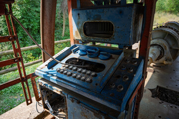 A close-up of the rusted, antique control panel inside an abandoned blue and red mining machinery operator's cabin, showing numerous buttons and dials