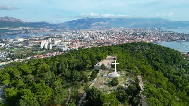 Panoramic aerial view of Split, Croatia, from Marjan Hill, featuring the iconic cross, Croatian flag, bustling city, and the serene Adriatic Sea.