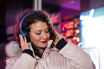 Fototapeta premium Cute charismatic curly hair girl in winter jacket outside, listening to music over headphones