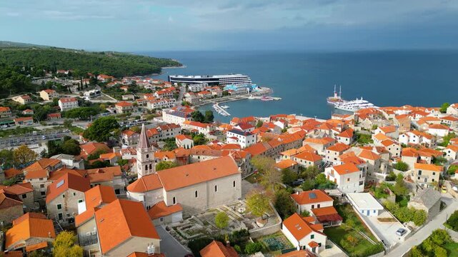 Aerial view of Postira, Brac Island, Croatia. Terracotta roofs meet the deep blue Adriatic under dramatic skies. A picturesque harbor town, blending history with modern tourism.