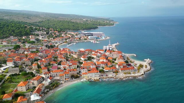 Aerial view of Postira, Brac Island, Croatia. Terracotta roofs meet the deep blue Adriatic under dramatic skies. A picturesque harbor town, blending history with modern tourism.