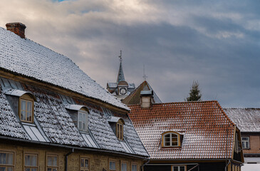 Snow dusted rooftops of old European town houses with clock tower under cloudy winter sky, traditional architecture cityscape background