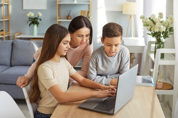 Mother, her son and daughter watching training video lesson, work on laptop computer, searching necessary information in internet, or enjoying online entertainment. Family and leisure