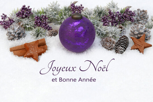 Carte de Noël : Joyeux Noël et bonne année ! Décoration hivernale avec bâtons de cannelle, baies, pommes de pin, branches de sapin et boules de Noël violettes dans un paysage enneigé.