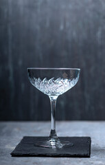 Elegant empty crystal coupe glass on a dark slate surface with moody lighting, perfect for cocktail, bar, and drink-themed visuals
