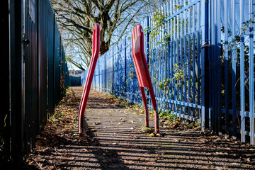 Bright red width restriction barriers along a sunlit pathway with blue fencing.