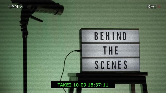 A cinematic view of a Behind the Scenes sign on a wooden stool under professional studio lighting. The frame includes a timestamp and recording elements mimicking a video camera interface. Close up.