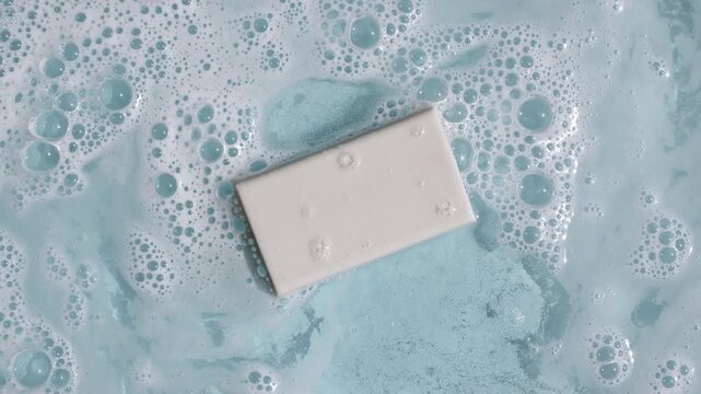 A bar of soap on a water surface with bubbles of white soapy foam. Concept of bath products, skin care products advertisement spa cosmetics. Body care and relaxation. High quality 4k footage