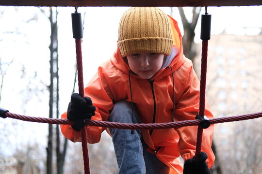 Child climbing rope net on playground in winter - Powered by Adobe