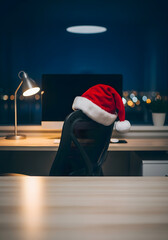 Escritorio minimalista con monitor apagado, lámpara de diseño y gorro de Papá Noel en silla de oficina, fondo corporativo navideño con espacio para texto