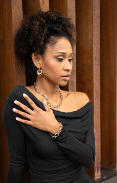 Young African-American woman, elegant with curly hair, dressed in black, posing and showing a necklace and thick chain earrings of modern and striking style.