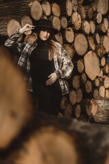 Peace of Motherhood: Pregnant woman, gently holding her belly, posing against the background of a natural pile of cut wood in the warm colors of autumn