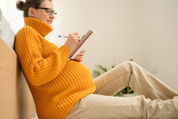 Expecting mother thoughtfully writing important delivery notes in her journal. Warm domestic scene...