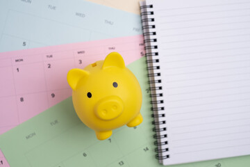 Piggy bank and notebook on calendar pages. Scheduled savings plan. 