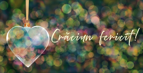 Poczt&oacute;wka bożonarodzeniowa - przezroczysta bombka choinkowa w kształcie serca na tle kolorowych rozmyć świateł bokeh z napisem Merry Christmas w języku rumuńskim
