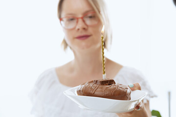 Pretty woman blowing candlelight on a chocolate donut, happy birthday celebration. 