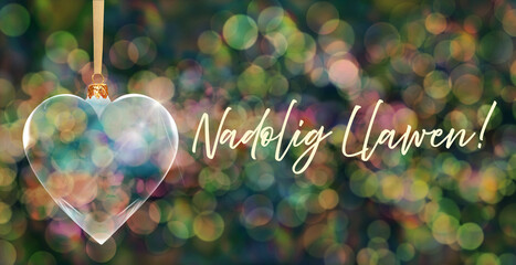 Poczt&oacute;wka bożonarodzeniowa - przezroczysta bombka choinkowa w kształcie serca na tle kolorowych rozmyć świateł bokeh z napisem Merry Christmas w języku walijskim