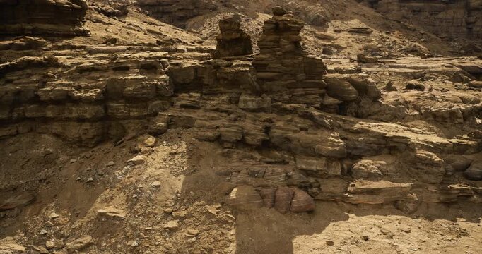 This rugged landscape features various rock formations, showcasing the effects of erosion. The dry, sandy ground reflects the harsh desert environment under bright daylight.
