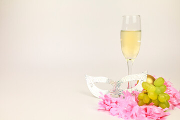 Champagne on classic champagne glass next to grapes, mask and pink garland