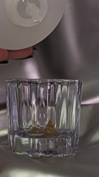 Oxidizer drip falling into glass cup with brow and lash tint in a beauty salon. Vertical video of drop of liquid falling into mixing cup used for brow and lash tint preparation in beauty studio