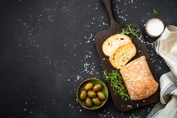 Ciabatta bread on wooden board with olive oil, olives and herbs.