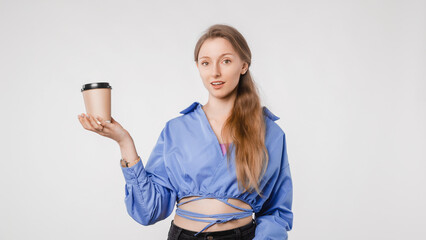 Young woman enjoying takeaway coffee cup looking at camera, standing against white backdrop, casual outfit, modern lifestyle concept