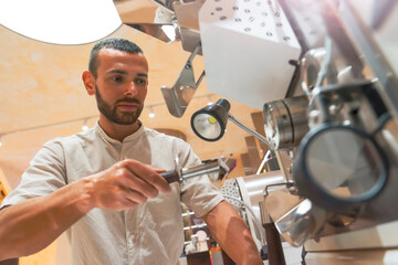 Worker is focused on preparing coffee beans using a roasting machine in a workshop setup dedicated to coffee production, highlighting the process of crafting a quality drink