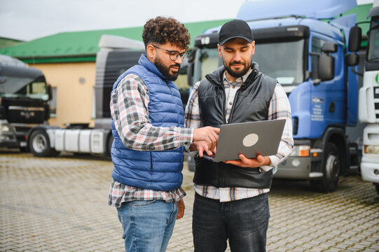 Truck drivers discussing logistics using laptop at fleet lot