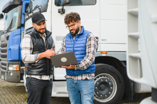 Truck drivers discussing logistics using laptop at fleet parking