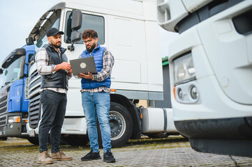 Truck drivers discussing logistics using laptop at depot