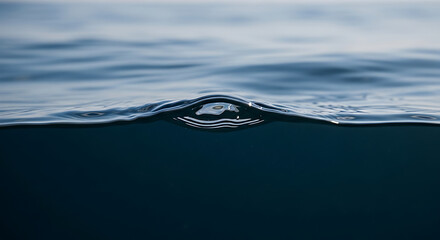 A solitary air bubble breaks the tranquil surface of the deep blue sea, a momentary disturbance creating a perfect dome on the water's edge
