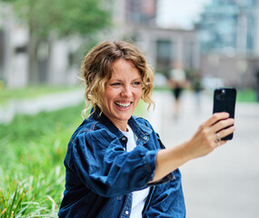 Portrait of a young woman girl taking a selfie with a smartphone mobile phone , having fun and laughing, walking city street