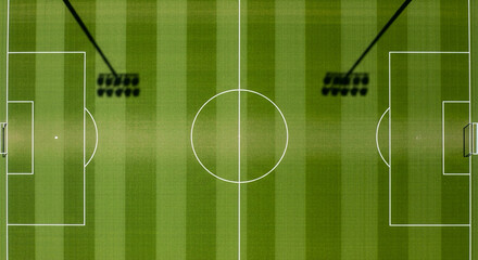 Overhead drone view of a perfectly marked football pitch, empty, sunlight casting shadows of goalposts, symmetrical composition.