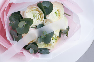 Minimalist bouquet with white ranunculus and eucalyptus leaves wrapped in pink paper and translucent ribbon
