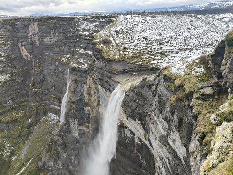 Majestuosa cascada del Salto del Nervión entre acantilados blancos y un paisaje invernal cubierto de nieve.