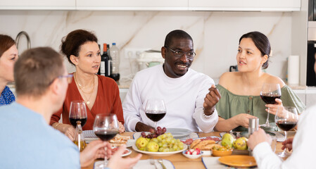 Happy middle-aged men and women sitting at table with a glass of wine while having friendly conversation at home