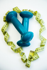 Blue dumbbells rest on a clean white surface, encircled by a measuring tape, representing fitness goals, healthy lifestyle choices, and motivation for exercise
