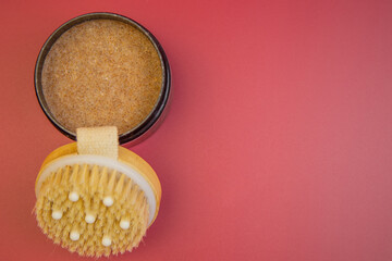 Spa essentials include a round jar filled with brown sugar scrub and a natural bristle body brush on a vibrant pink background, ideal for wellness and relaxation themes