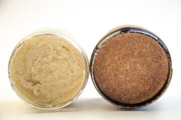 Two jars of body scrubs, one creamy and light, the other coarse and dark, highlighting natural skincare products for exfoliation and self-care routines