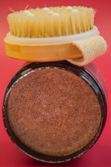 Body scrub in a glass jar with a wooden lid and brush, highlighting the rich texture of the product, placed on a vibrant red background, ideal for skincare enthusiasts