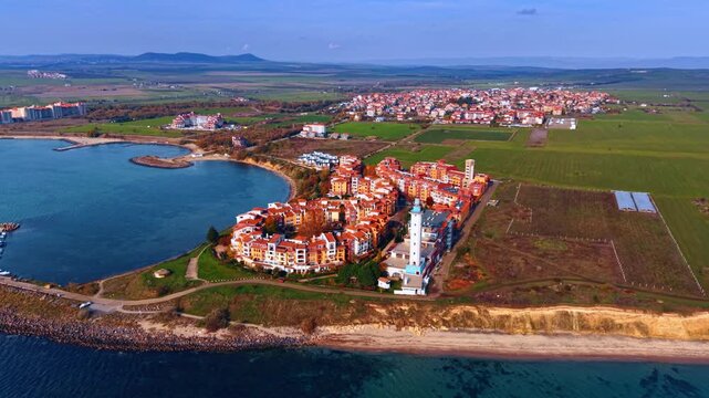 Lovely residential complex of bright houses and lighthouse at the shore of the sea. Green fields around the area. Aheloy, Bulgaria.