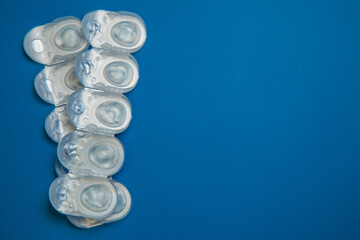 Many daily contact lenses in a disposable protective case in which clear lenses float lie on the side on a blue background with space for text. The concept of ophthalmology, vision correction, eye