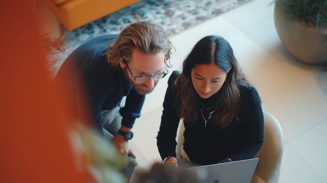 Dynamic duo collaborating on laptop in modern workspace