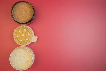 Three jars showcasing natural skincare products, featuring a sugar scrub, body butter, and exfoliating cream, set against a bright red backdrop with copy space for text