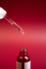 Glass dropper releasing serum from bottle against a vivid red backdrop, emphasizing skincare application and the essence of beauty and wellness in a captivating scene