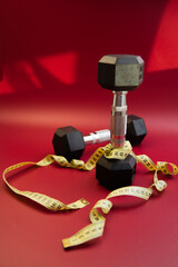 Dumbbells positioned on a striking red surface, with a measuring tape wrapped around them, representing fitness goals, health awareness, and dedication to physical improvement