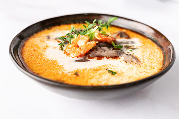  Fresh aromatic hot Thai soup Tom Yum with mushrooms, shrimps and different spices on white marble background close up. Tasty food concept.